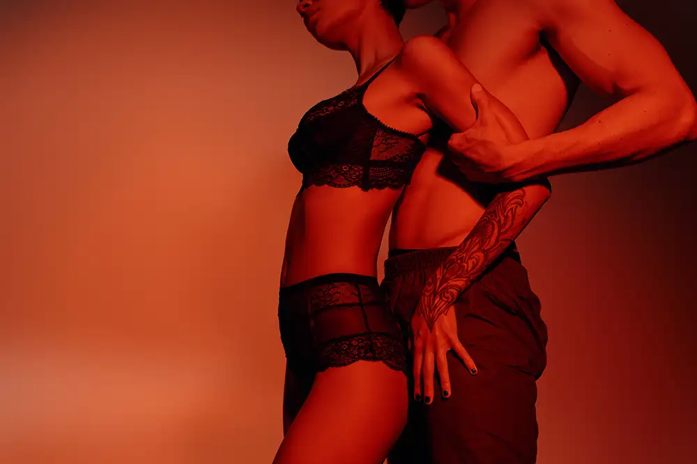 Couple in black lingerie posed together with dramatic red lighting