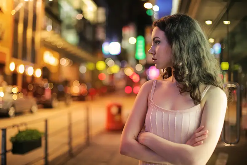 Young woman in sleeveless dress stands on bustling city street at night